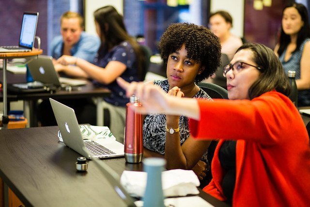 A student points at the board as she talks to the woman sitting next to her.